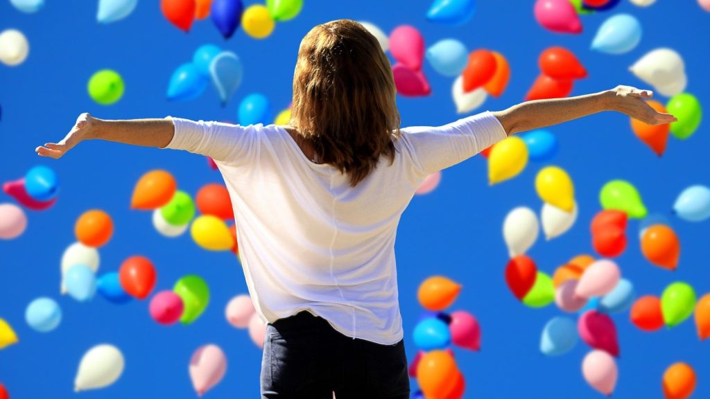 vergroot je zelfvertrouwen. Een vrouw staat met haar rug naar de camera en kijkt blij naar een blauwe lucht met ballonnen