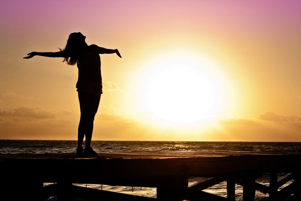 Vrouw met wie het heel goed gaat, strekt haar armen uit bij zonsondergang.