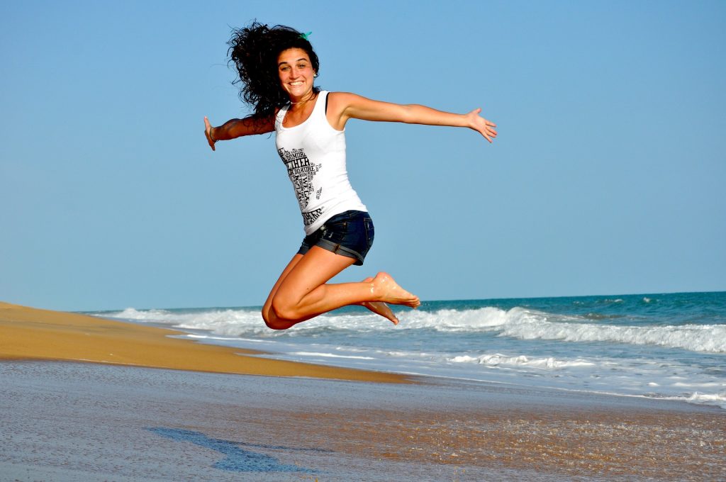 Vrouw die blij is en een gat in de lucht springt op het strand