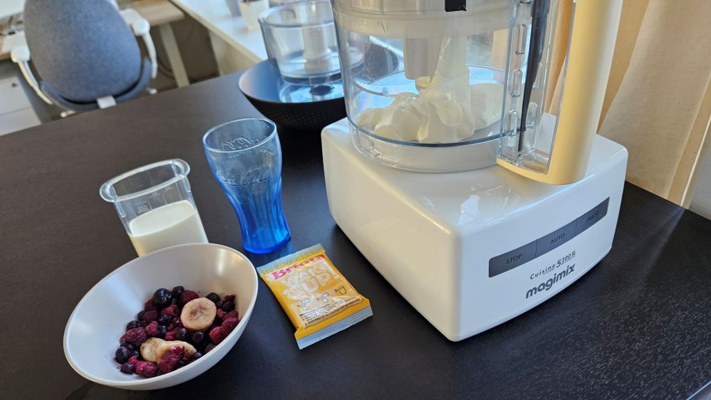 Fruit in een schaaltje, melk, een zakje Brinta en een glas naast de foodprocessor.